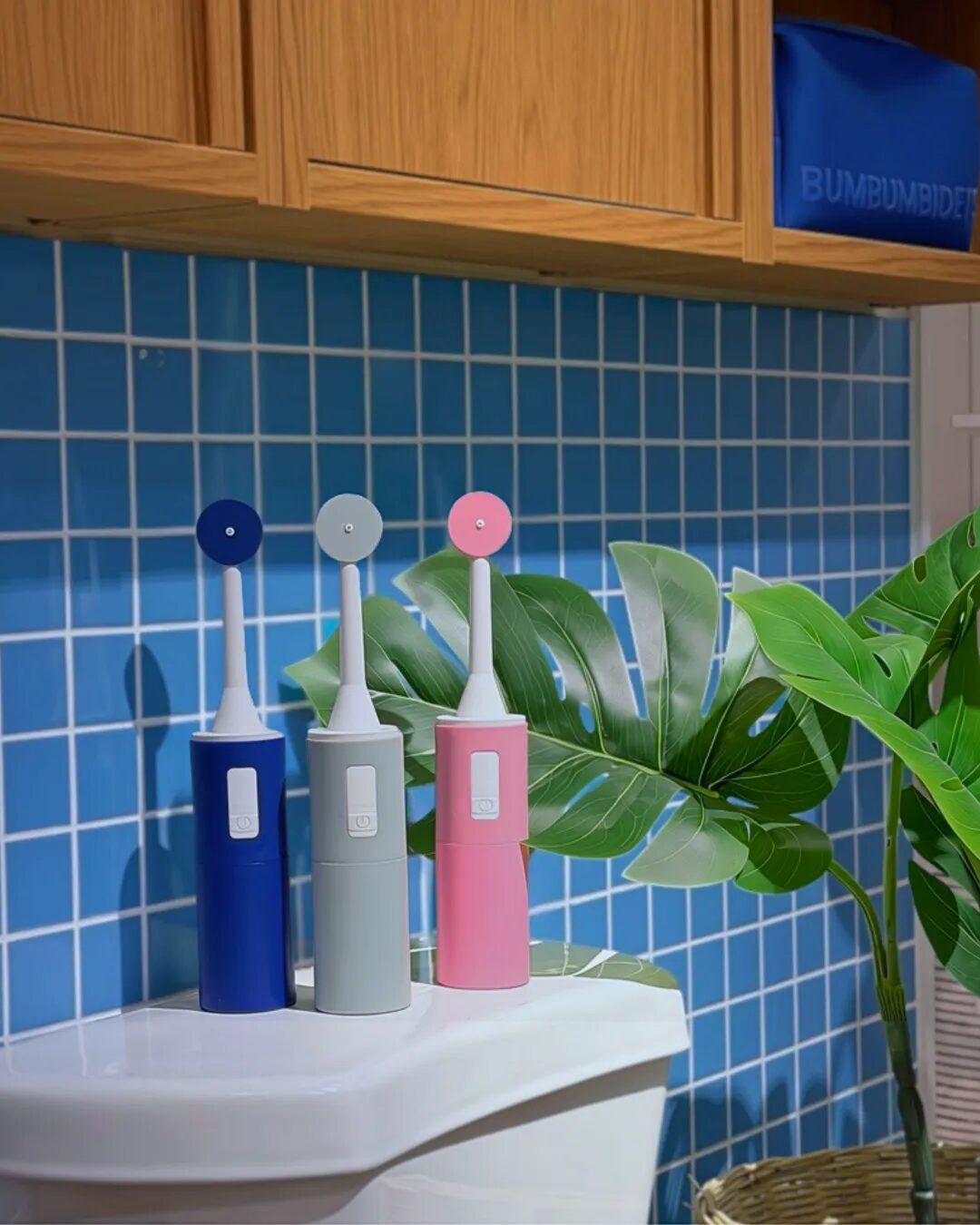 BumBum portable rechargeable bidets in blue, gray and pink on a toilet tank