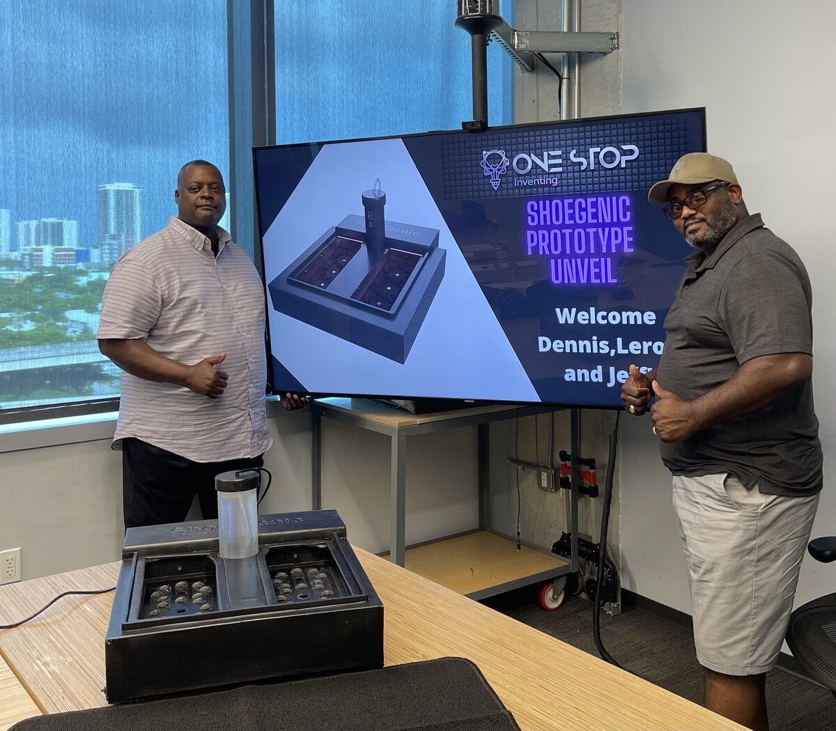 Two inventors beside a shoe prototype and a One Stop Inventing presentation screen
