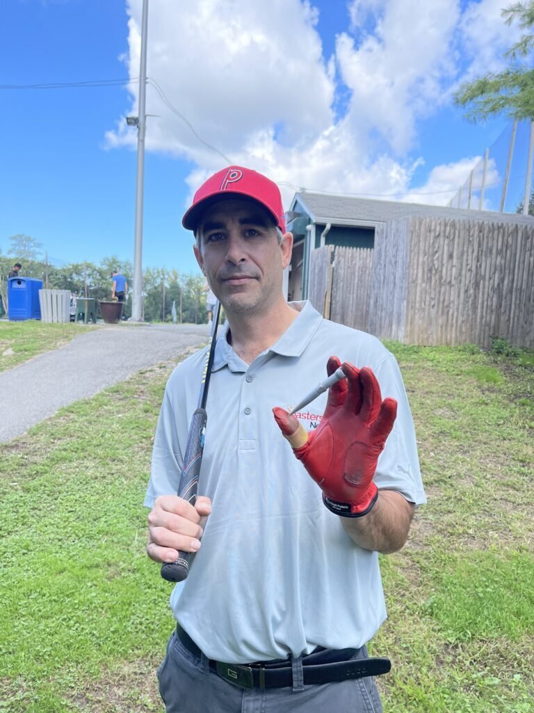 Inventor outdoors wearing a red cap and holding a prototype component
