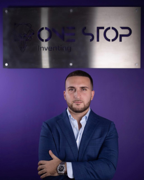 Portrait of Jose in a suit standing beneath the One Stop Inventing sign